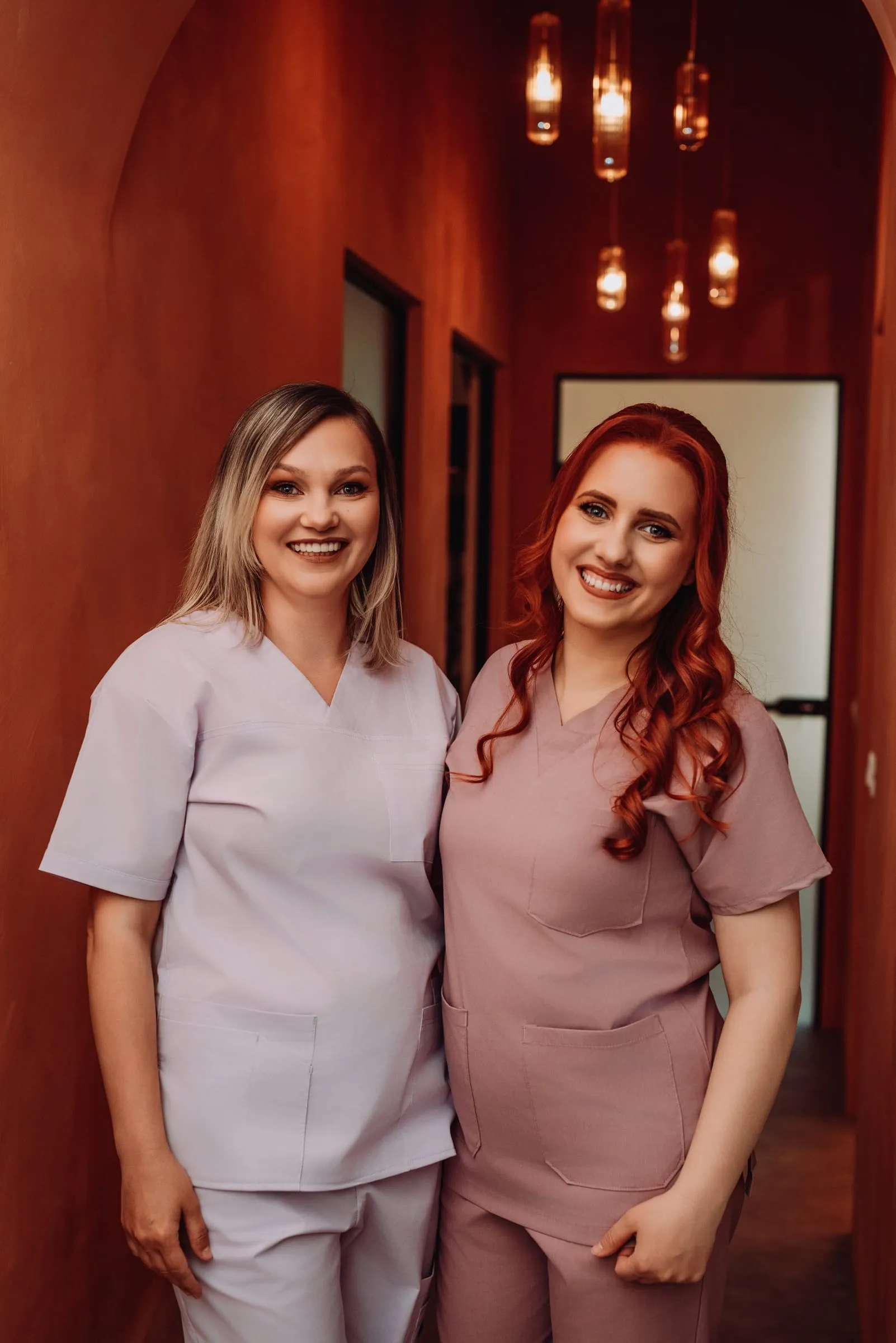 Două medici Cocard zâmbind pe holul cu arcade și lumini calde al clinicii
